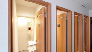 Un couloir d’hôtel avec des portes en bois, une salle de bain visible avec un lavabo et des articles de toilette, et une source de lumière vive à l’arrière-plan.