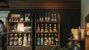 A bar with shelves of various liquor bottles, a wooden counter, and a metal barrel. - Negura (Ogimi)