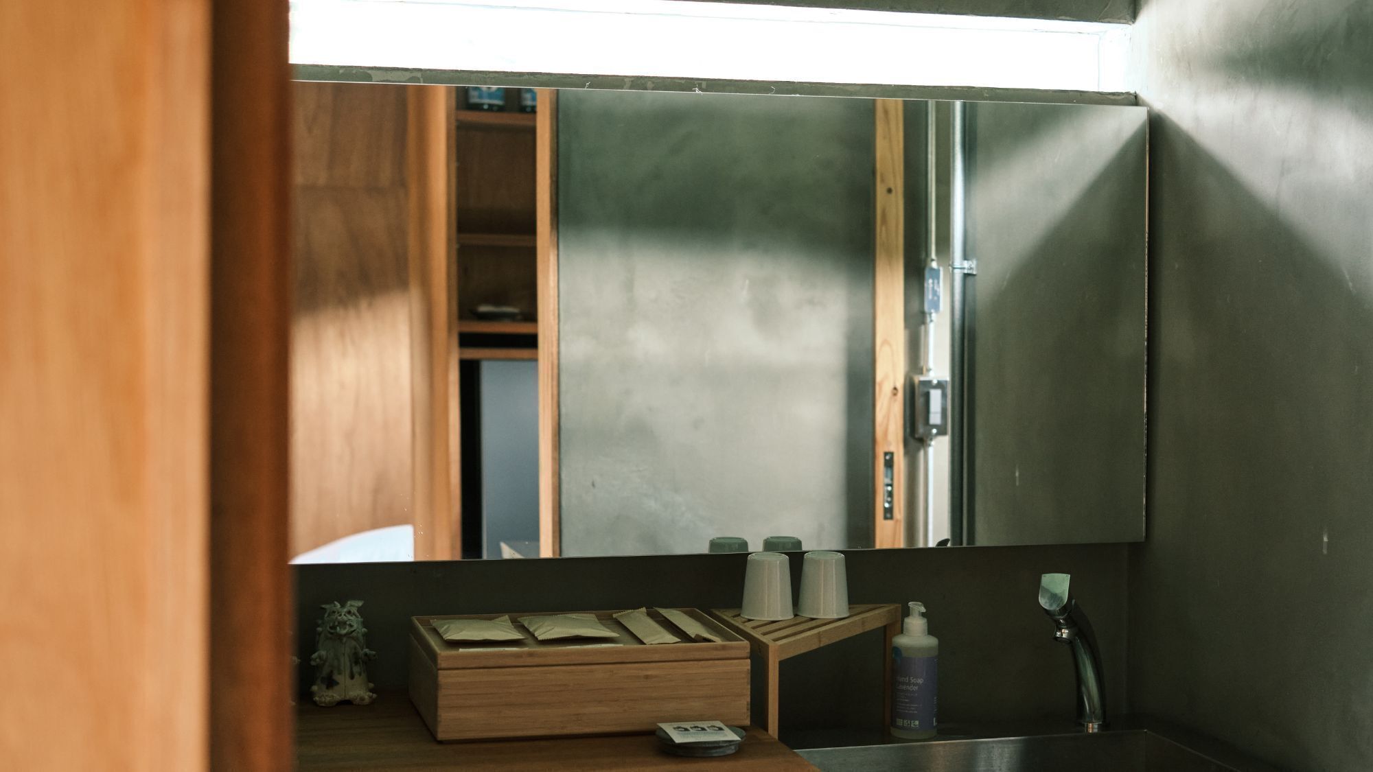 A bathroom with a wooden vanity, a mirror, a sink, and a bottle of hand soap.
