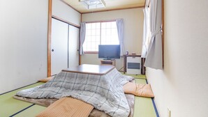 A traditional Japanese room with tatami flooring, a futon bed, a television, and a heater. - Pension Silver Fern (Otari)