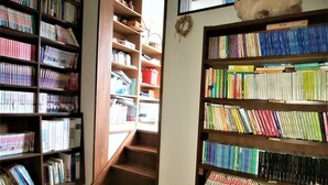 A library with bookshelves filled with books, a staircase, and a small statue on the top shelf. - Pension Silver Fern (Otari)