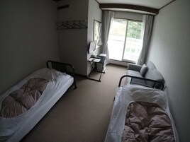 Quarto de hotel com duas camas de solteiro, uma escrivaninha, uma cadeira e janela com cortinas.