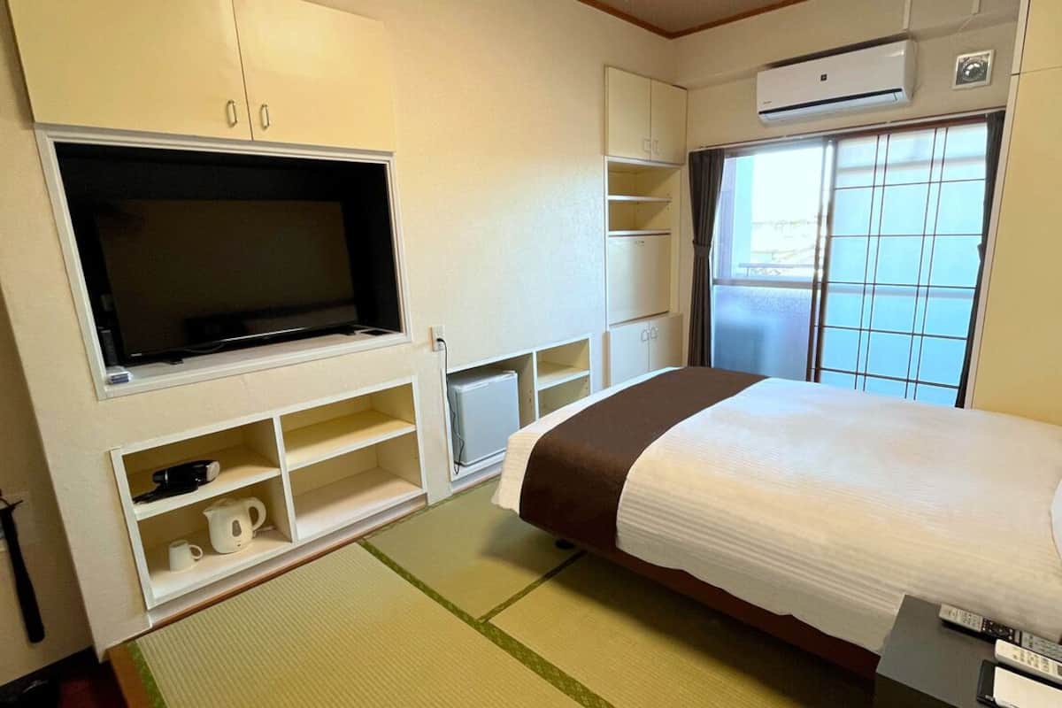 Une chambre d’hôtel avec un lit, une télévision, une étagère contenant des ustensiles de cuisine et une fenêtre donnant sur un paysage agréable.