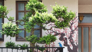 Ein Gebäude mit einer Wandmalerei von Baum und Blumen, einem schwarzen Metallzaun und einem Vogel, der auf dem Zaun sitzt.