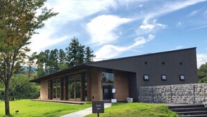 A modern building with large glass windows, a stone wall, and a sign indicating a shop.