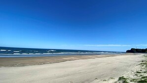 A wide beach with a clear sky and ocean waves.