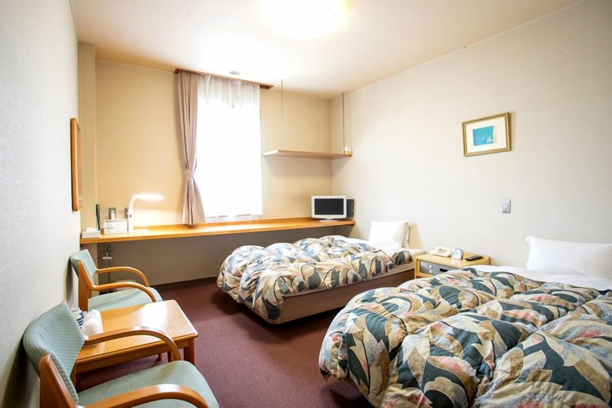 A hotel room with two beds, a desk, a chair, a television, and a window with curtains.