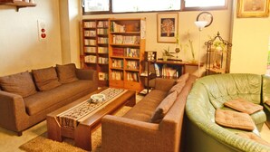 A living room with a brown sofa, a green sofa, a wooden coffee table, and a bookshelf filled with books. - Hotel Irihama (Sakaide)