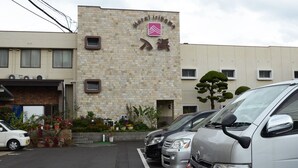 A hotel with a stone facade, a sign with Japanese characters, and a parking lot with cars. - Hotel Irihama (Sakaide)