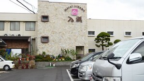A building with a sign reading "Hotel irihama" and a logo. There are parked cars in front and a small garden area with plants and flowers. - Hotel Irihama (Sakaide)