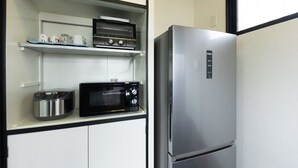 A compact kitchen with a stainless steel refrigerator, a microwave, and a toaster oven on a white cabinet. - Iu Workation (Ito)