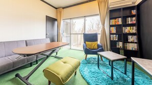 A modern living room with a sofa, a dining table, a small ottoman, a bookshelf, and a chair with a yellow cushion. - Iu Workation (Ito)