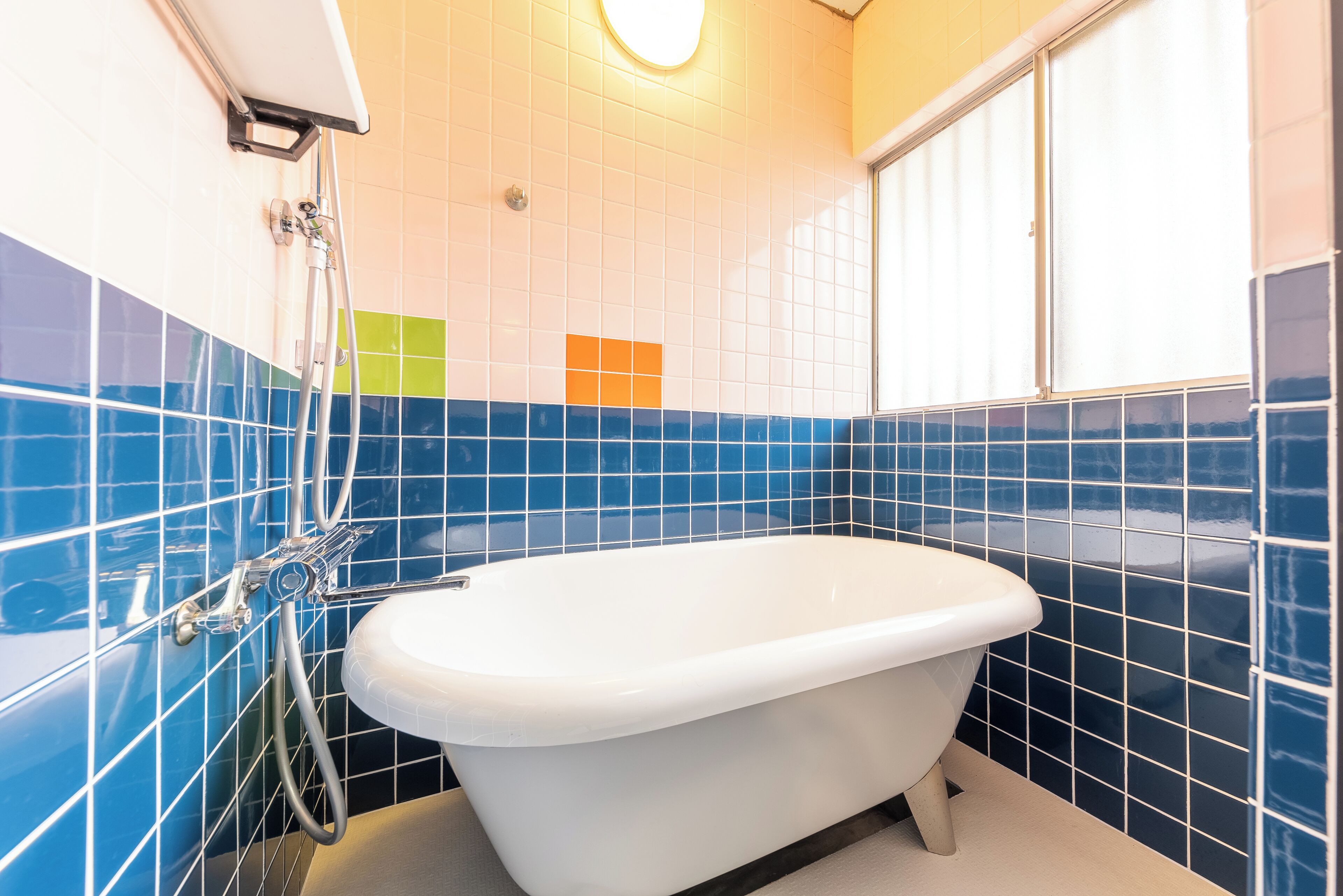 A bathroom with a white bathtub, blue and white tiled walls, and a window.