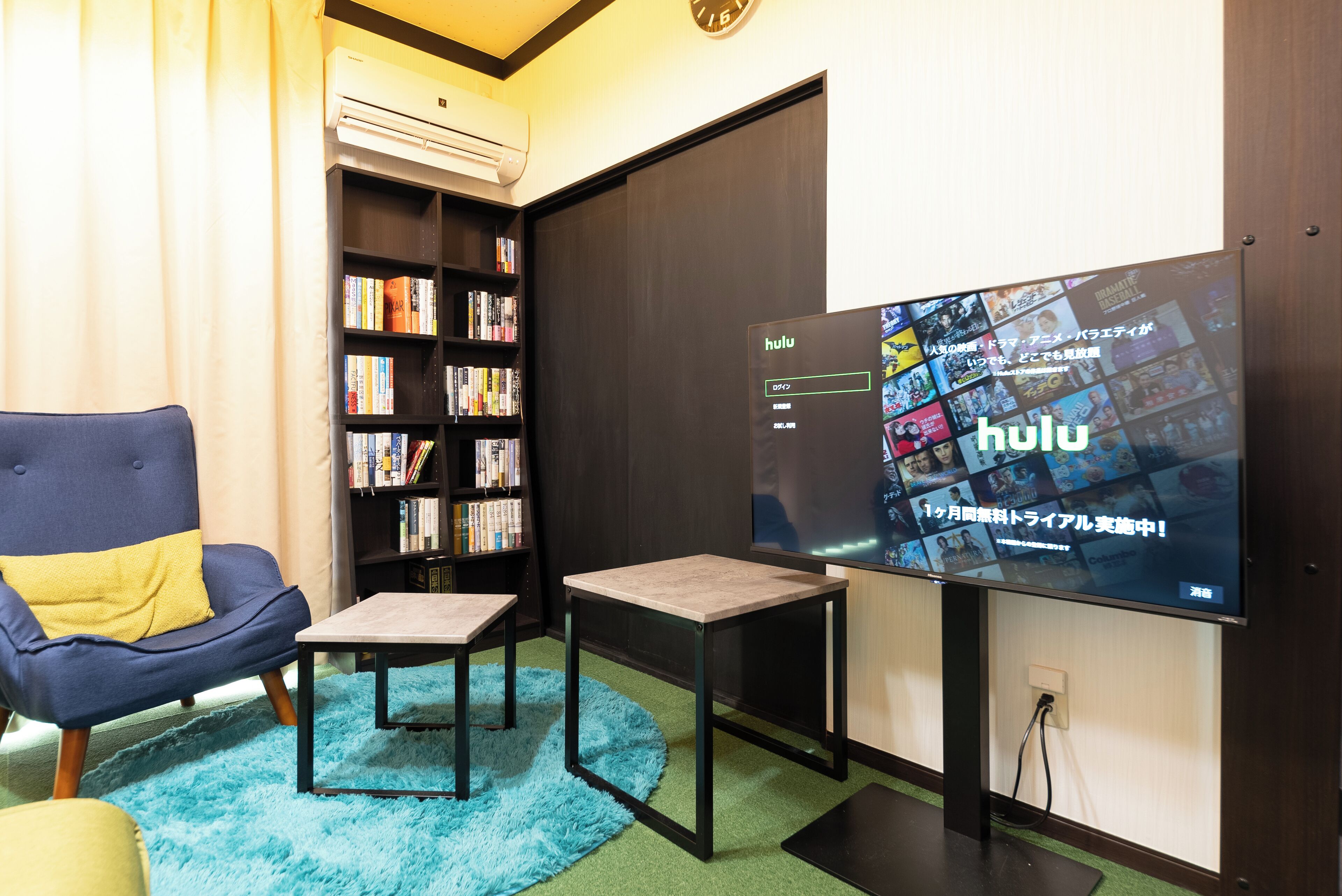 A modern living room with a large flat-screen TV displaying Hulu, a bookshelf, a blue armchair, and a small coffee table.
