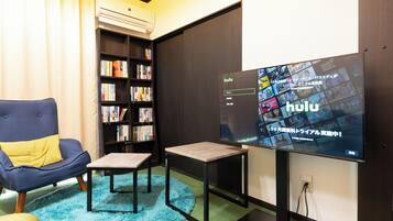 A modern living room with a large flat-screen TV displaying Hulu, a bookshelf, a blue armchair, and a small coffee table.