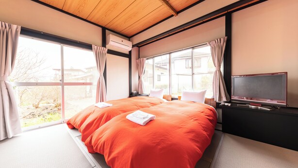 A hotel room with a large bed, a TV, and a window with curtains. - Iu Workation (Ito)