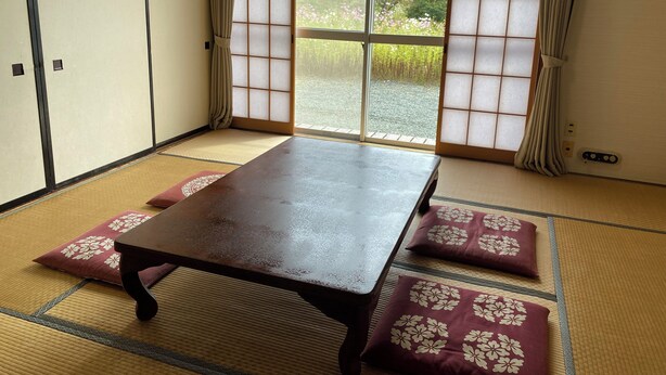 A tatami mat room with a wooden table, cushions, sliding shoji doors, and a view of greenery outside. - Edogawa Garden (Iwaki)