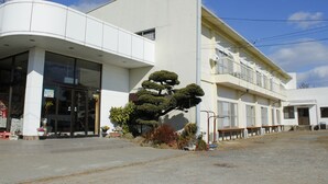 A modern building with a curved facade, large windows, and a small tree in the front. - Edogawa Garden (Iwaki)