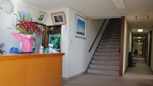 A reception area with a wooden counter, a staircase, and framed pictures on the wall. - Edogawa Garden (Iwaki)