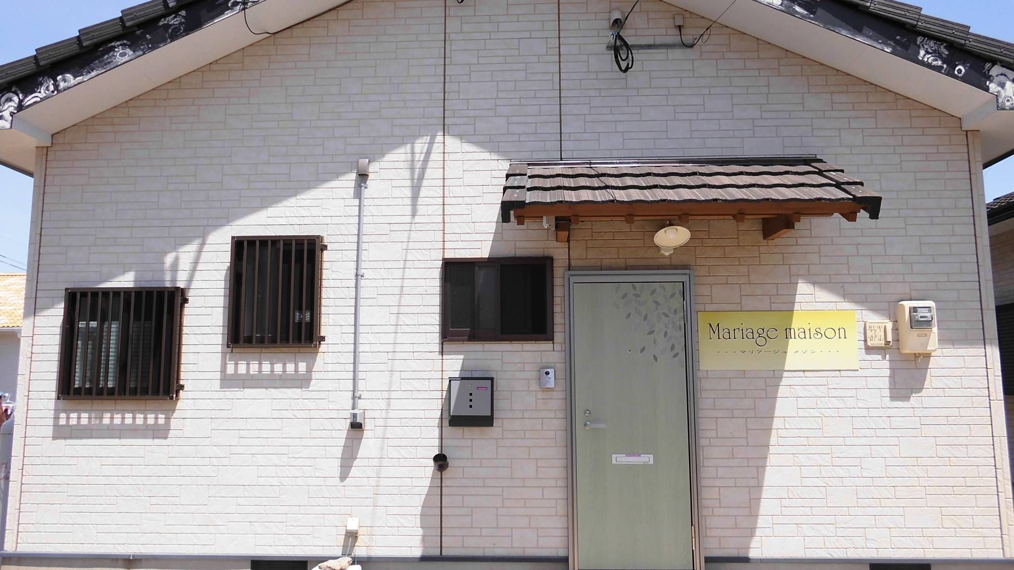 A building with a tiled roof, a green door, and a sign that reads "Mariage maison".