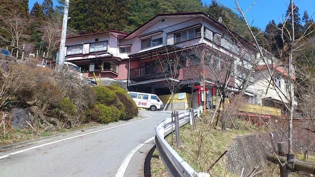 Un immeuble de deux étages avec un balcon à l’étage supérieur, une allée et un fourgon blanc garé devant.