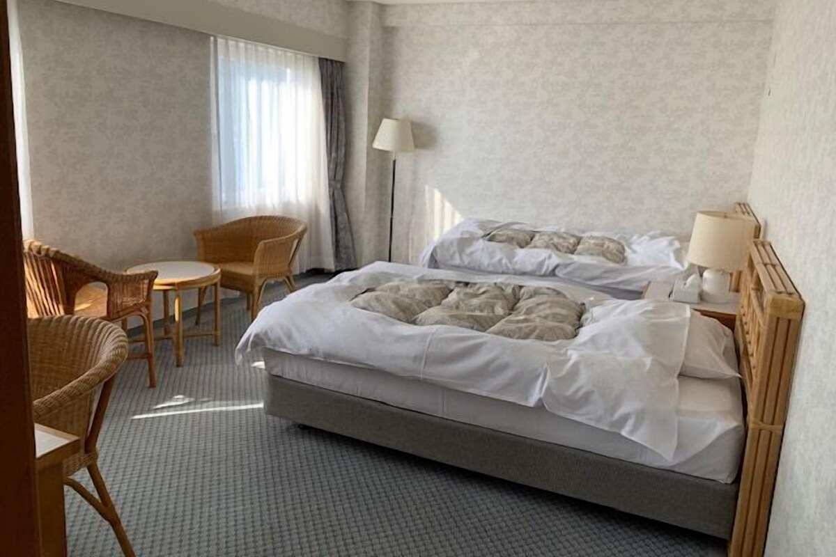Una habitación de hotel con una cama grande, dos sillas, una mesita y una lámpara.