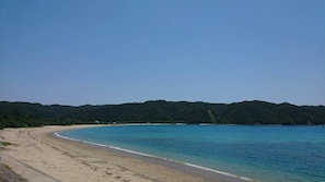 A beach with clear blue waters and a sandy shore, surrounded by green hills. - Amami no Yado Good Green (Setouchi)