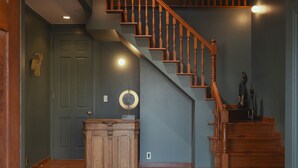 A staircase with wooden balusters, a wooden cabinet, and a rug with shoes. - The Rura (Maebashi)