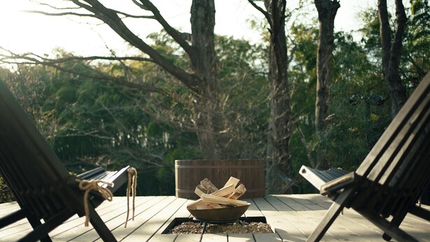 A wooden deck with a fire pit in the center surrounded by lounge chairs. - The Rura (Maebashi)