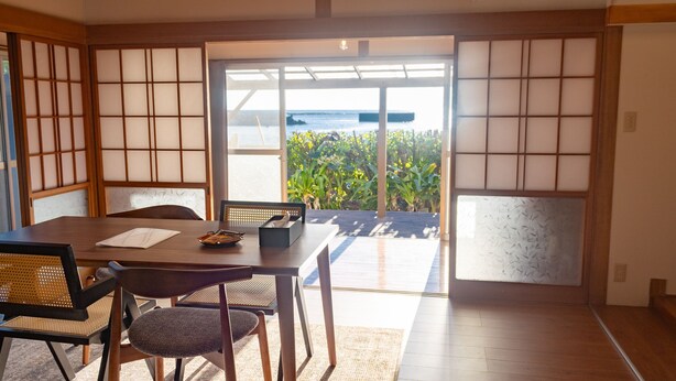 Ein traditioneller japanischer Raum mit Tatami-Böden, einer Schiebetür, die auf einen Balkon mit Meerblick führt, und einem niedrigen Tisch mit Kissen und einer kleinen Ablagefläche.