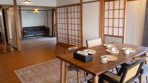 Ein traditioneller japanischer Raum mit Tatami-Bodenbelag, einem niedrigen Tisch gedeckt mit Tassen und einer Papiertauschbox, sowie einer Schiebetür mit Gittermuster.