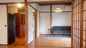 Ein traditioneller japanischer Raum mit Tatami-Böden, einem grauen Sofa, einem kleinen Tisch und einer hängenden Leuchte.