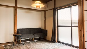 Ein modernes Wohnzimmer mit grauem Sofa, einem kleinen Beistelltisch und einem großen Fenster mit Holzrahmen.