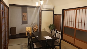 A traditional Japanese room with tatami flooring, a low table with chairs, a shoji screen, and a mounted air conditioner. - Moritasanchi (Ine)