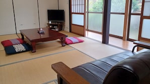 A traditional Japanese room with tatami flooring, a low wooden table, a sofa, and a television. - Moritasanchi (Ine)