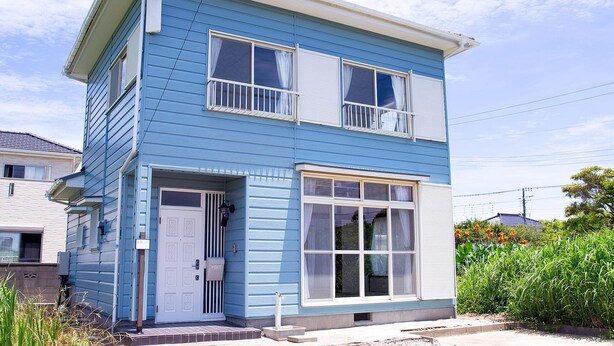 Una casa azul de dos pisos con una puerta blanca, un ventanal grande y un buzón.