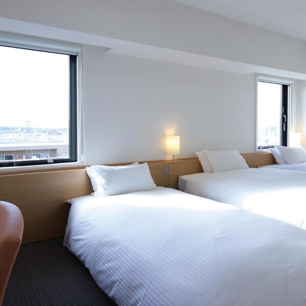 Una habitación de hotel con dos camas, una ventana y una mesita de noche con lámpara.