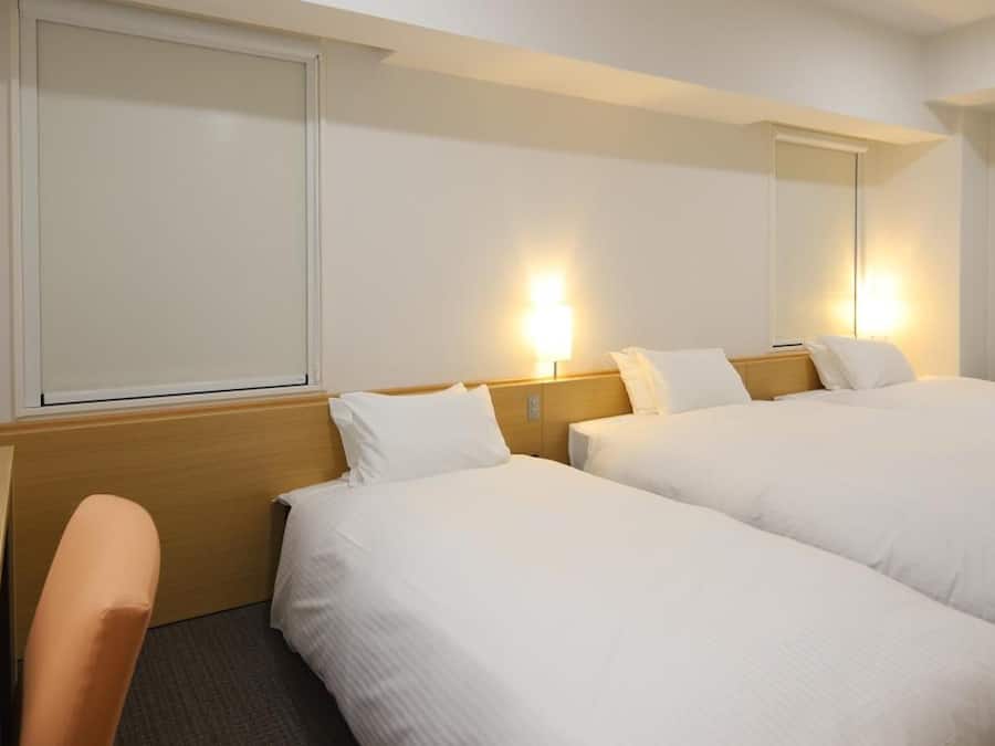 A hotel room with two beds, a wooden headboard, a desk, and a chair.