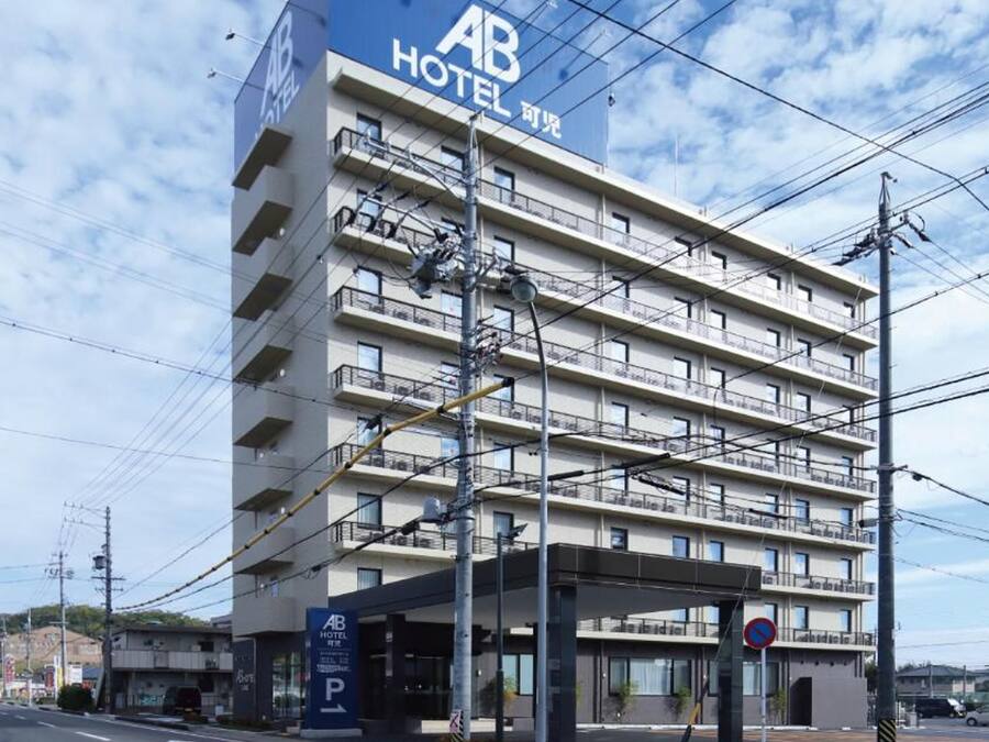 Un hotel a più piani con un evidente cartello 'AB HOTEL', un'area di parcheggio e un attraversamento pedonale.
