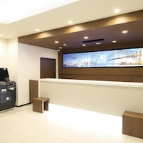 A hotel reception area with a large digital screen displaying a cityscape, a reception desk, and a self-service kiosk.