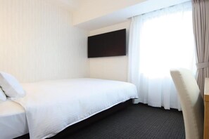 Une chambre d’hôtel avec un lit, un téléviseur à écran plat fixé au mur et une fenêtre avec des rideaux.