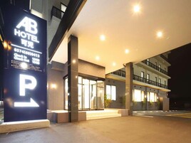 Entrada de hotel con un cartel llamativo de 'P' para estacionamiento, una zona de recepción y una fachada de edificio moderna.