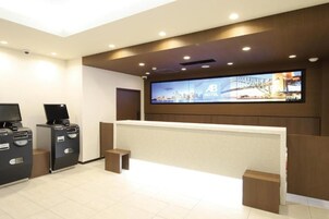Zona de recepción de un hotel con pantalla digital, mostrador de recepción y dos quioscos de autoservicio.