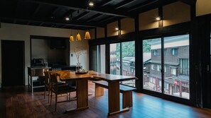 A modern kitchen with a wooden table and chairs, a coffee machine, and a large window overlooking a residential area. - Nipponia Hakusanshiramine Okuyamabitonosato Sennyomoto (Hakusan)