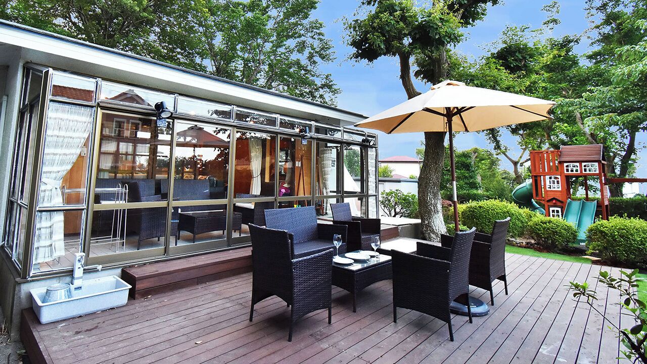 An outdoor patio with a glass-enclosed dining area, wooden deck, and a children's play structure.