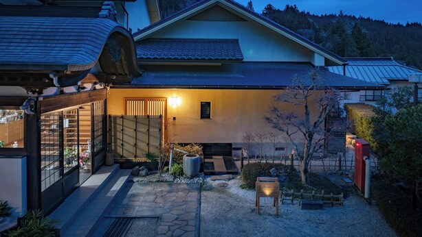Un edificio japonés tradicional con techo de tejas, entrada de madera y un camino de piedra que conduce a la puerta.