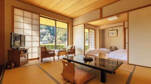 A traditional Japanese-style room with tatami flooring, a low table, a television, and a bed with white bedding. - Temple Hotel Matsui-bo (Minobu)