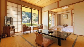 Ein traditionell gestalteter japanischer Raum mit Tatami-Bodenbelag, einem niedrigen Tisch, einer Couch und einem Bett.