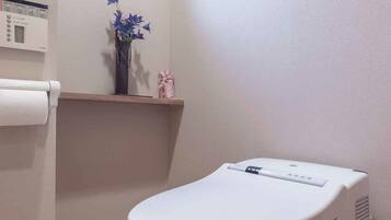 Ein Badezimmer mit Toilette, einem Fenster, einer kleinen Ablage mit Dekoration und einem Wandheizkörper.