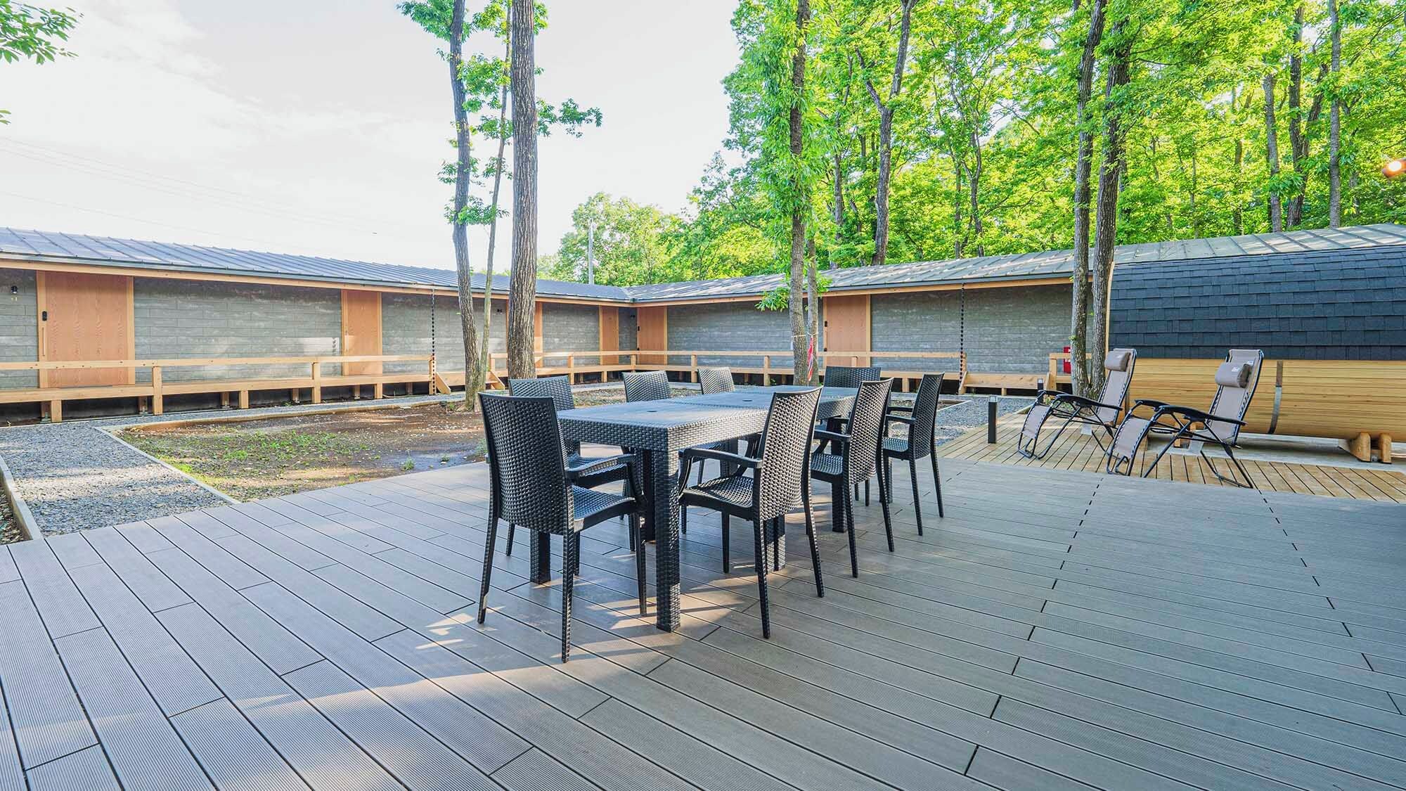 A deck with outdoor furniture, a covered area with a table and chairs, and a building with a sloped roof.